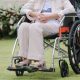 Elderly person seated in a wheelchair helped by a standing person in back of the chair