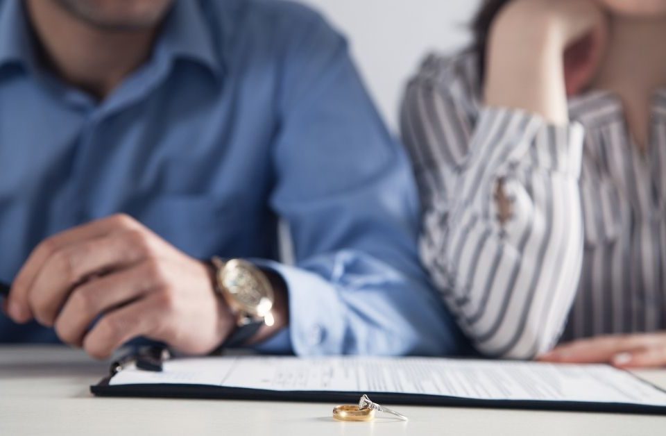 A man and woman seen from below the head with a divorce contract and a ring on a desk in front of them