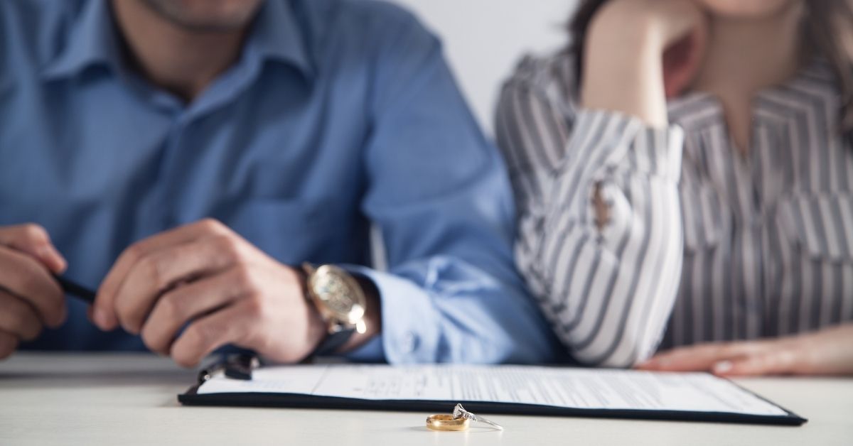 A man and woman seen from below the head with a divorce contract and a ring on a desk in front of them