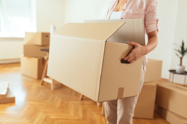 A woman is lifting a box. She is surrounded by moving boxes.