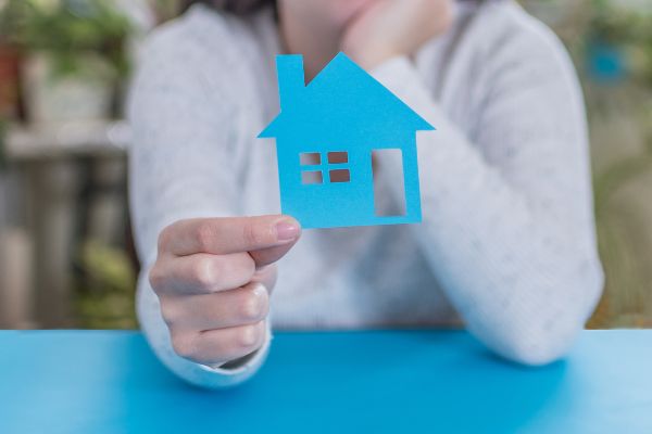 A woman holding up a cutout of a house to symbolize selling property